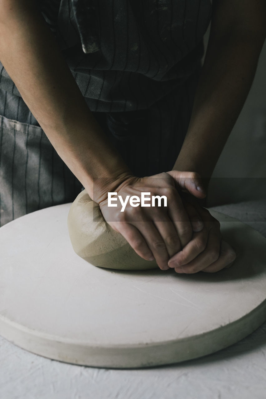 Midsection of craftswoman kneading clay in workshop