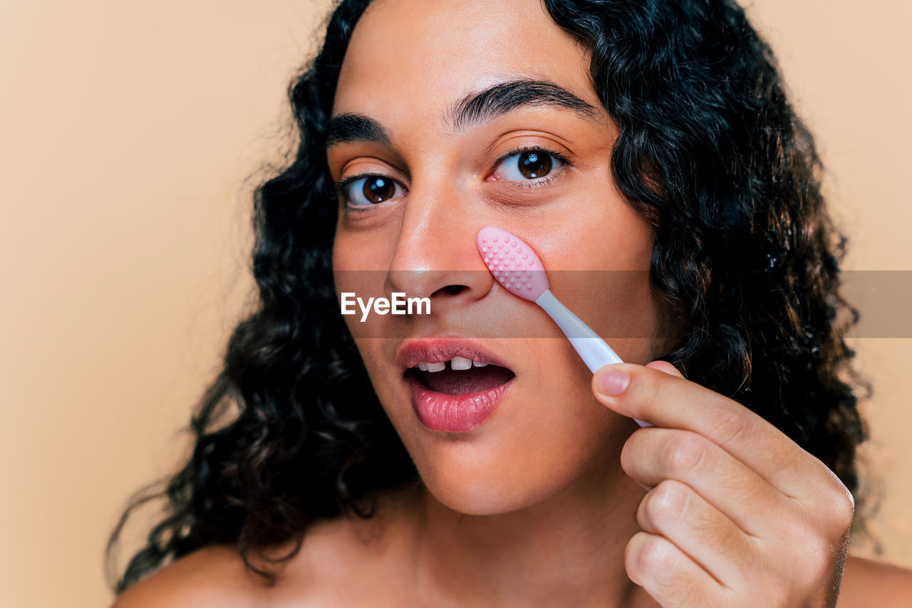 close-up of young woman applying make-up against yellow background