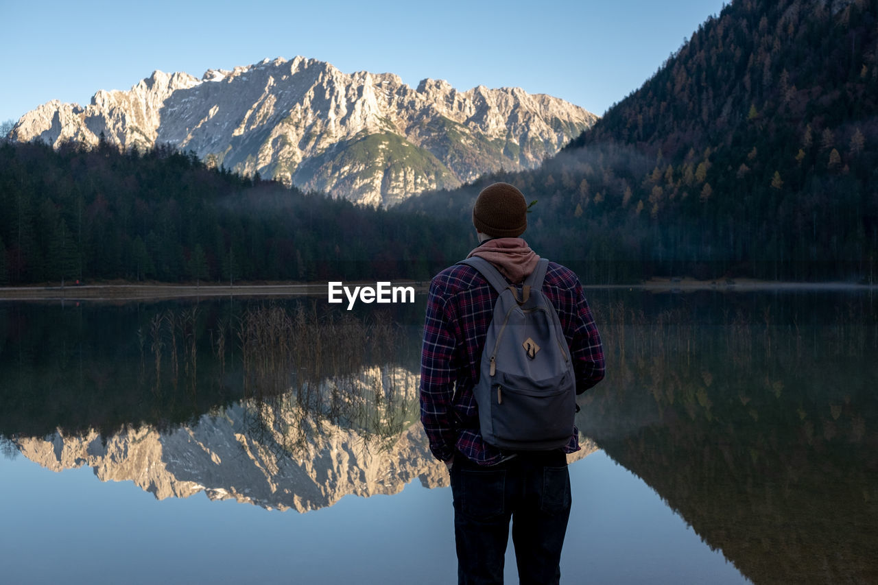 Rear view of man standing by lake against mountains