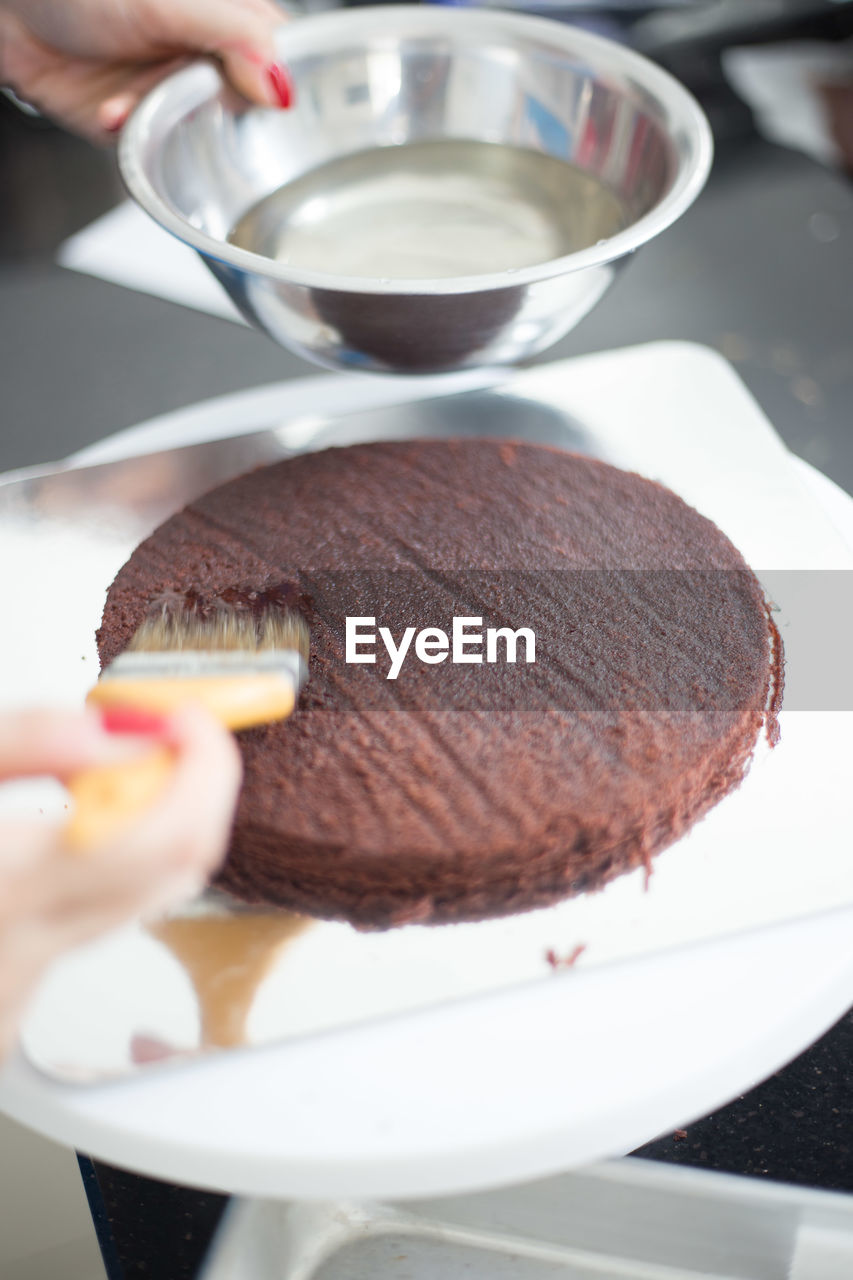 Cropped image of hand applying syrup on sponge cake