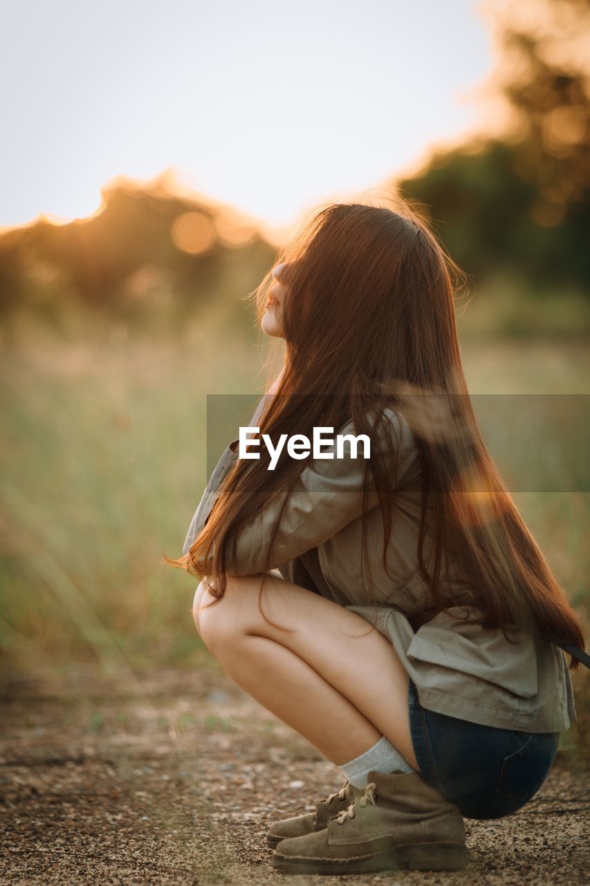 Side view of young woman crouching on field