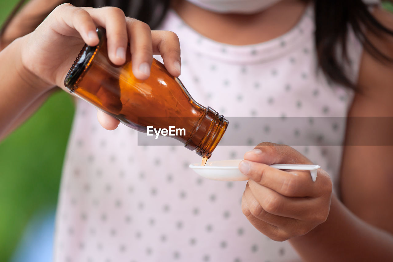 Midsection of girl pouring syrup in spoon