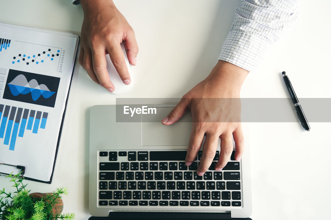 Cropped hands of businessman using laptop on desk