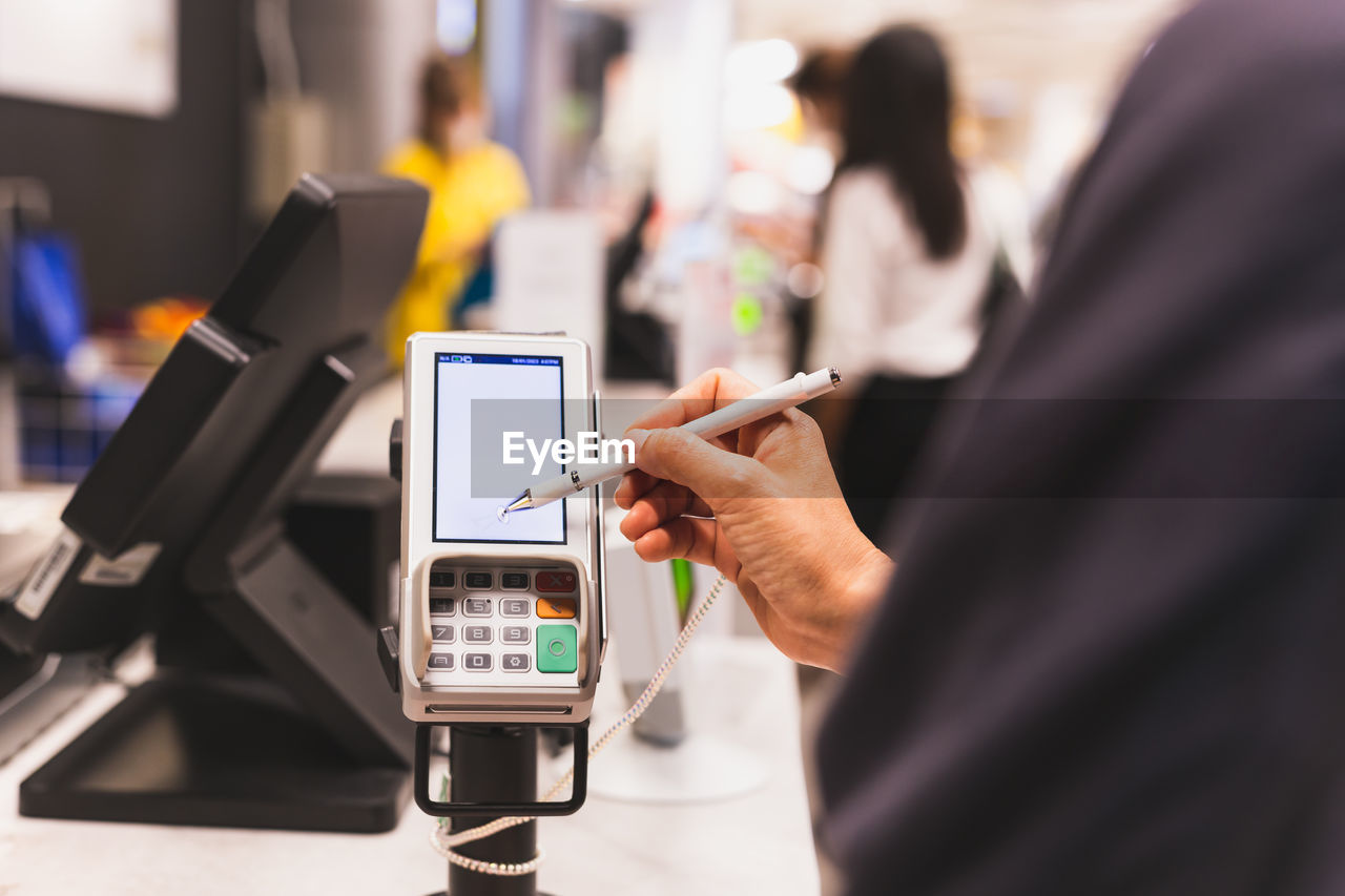 Consumer's women signing on a touch screen of credit card transaction machine at supper market.