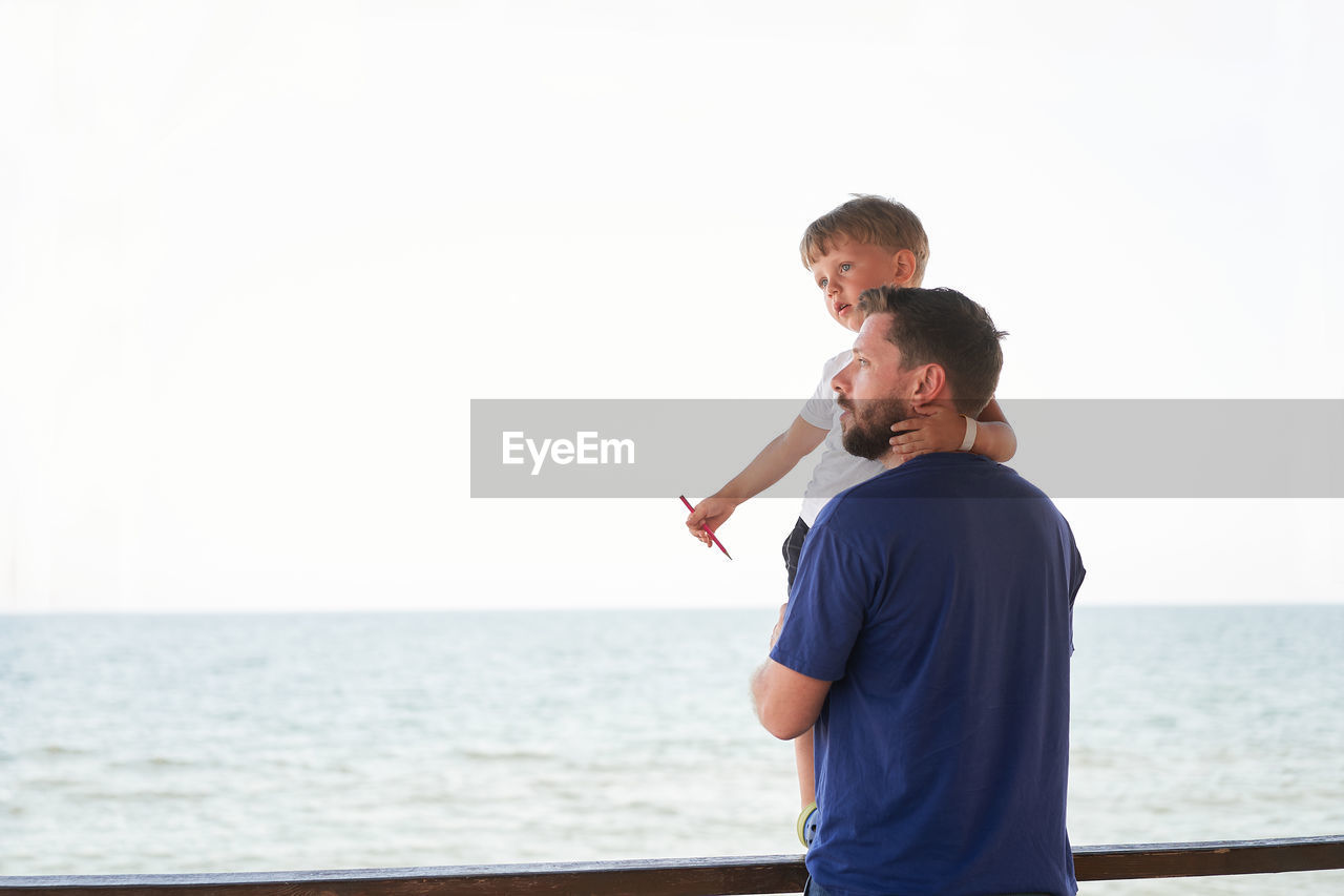 Father and son standing against sea