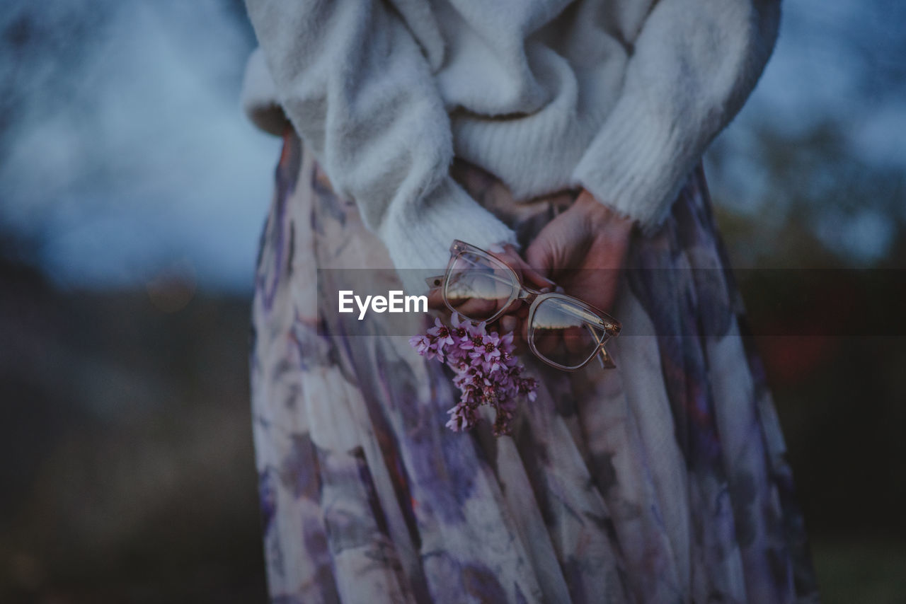 Close-up of hand holding purple flower and eyeglasses