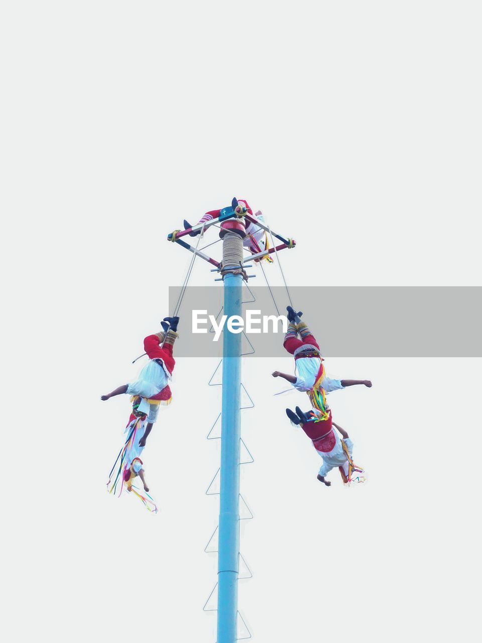 Low angle view of performers hanging on pole against clear sky