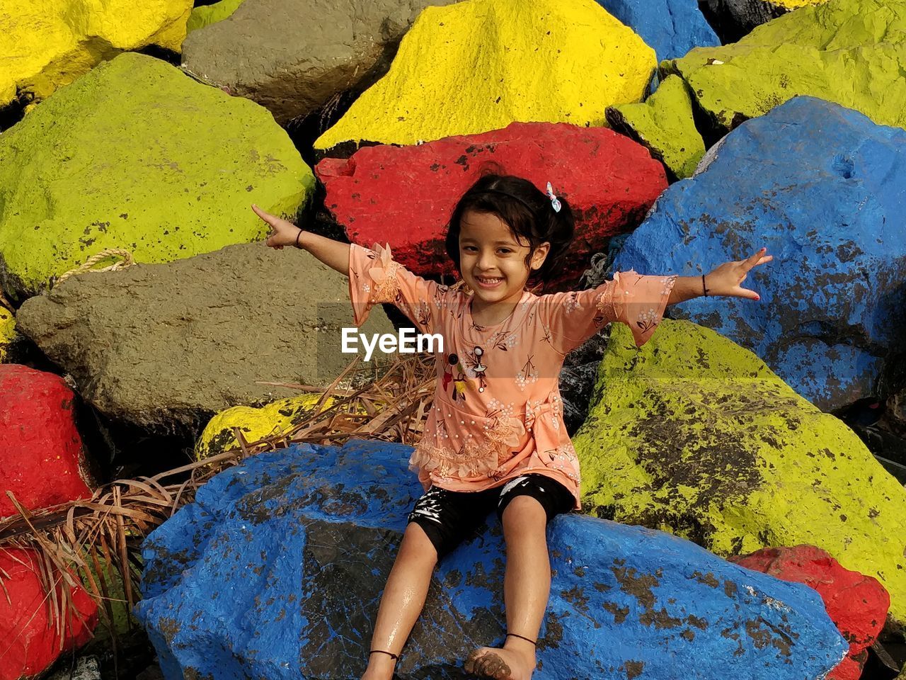 Full length portrait of smiling girl sitting on colorful rocks at beach