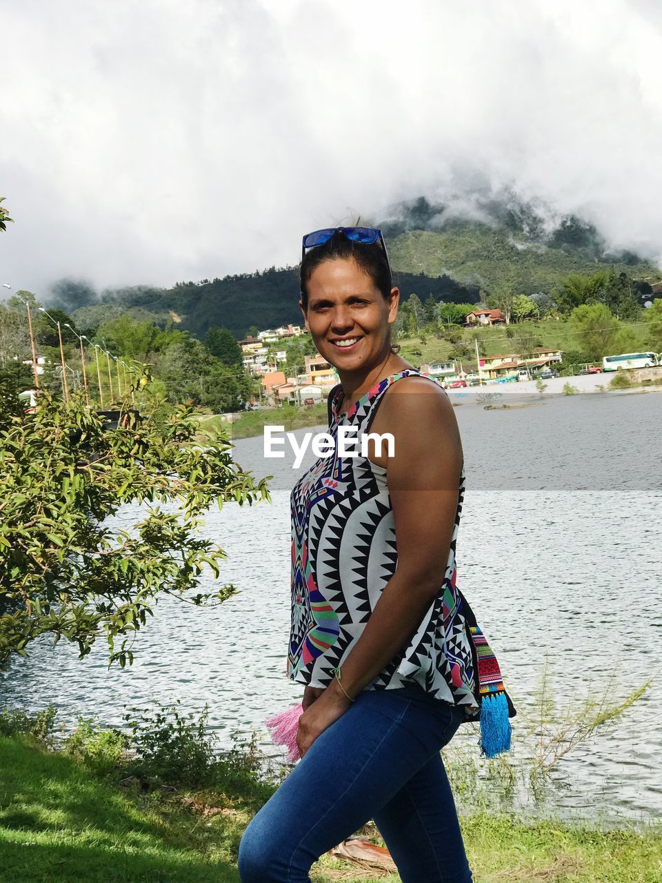 Portrait of smiling mid adult woman standing by lake against cloudy sky