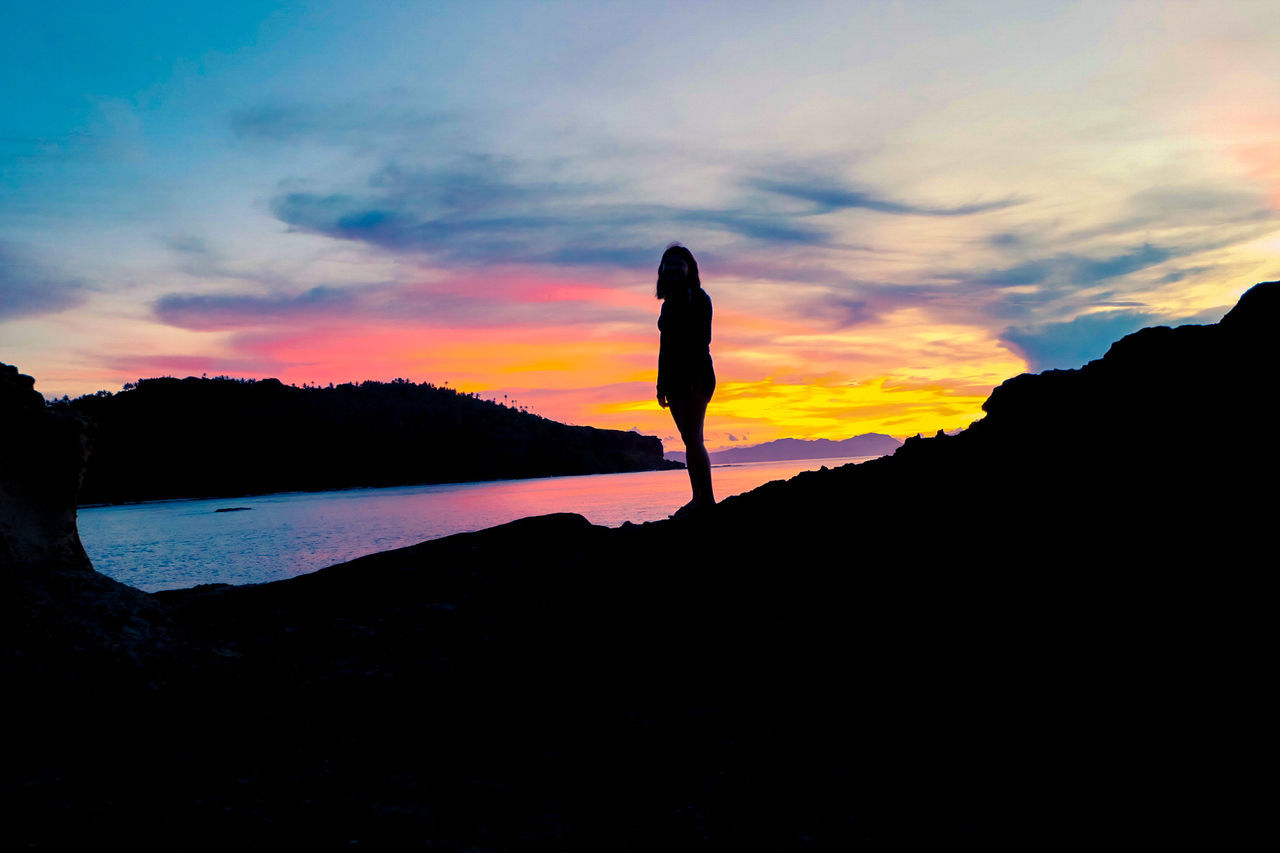 SILHOUETTE WOMAN STANDING BY WATER AGAINST SKY DURING SUNSET