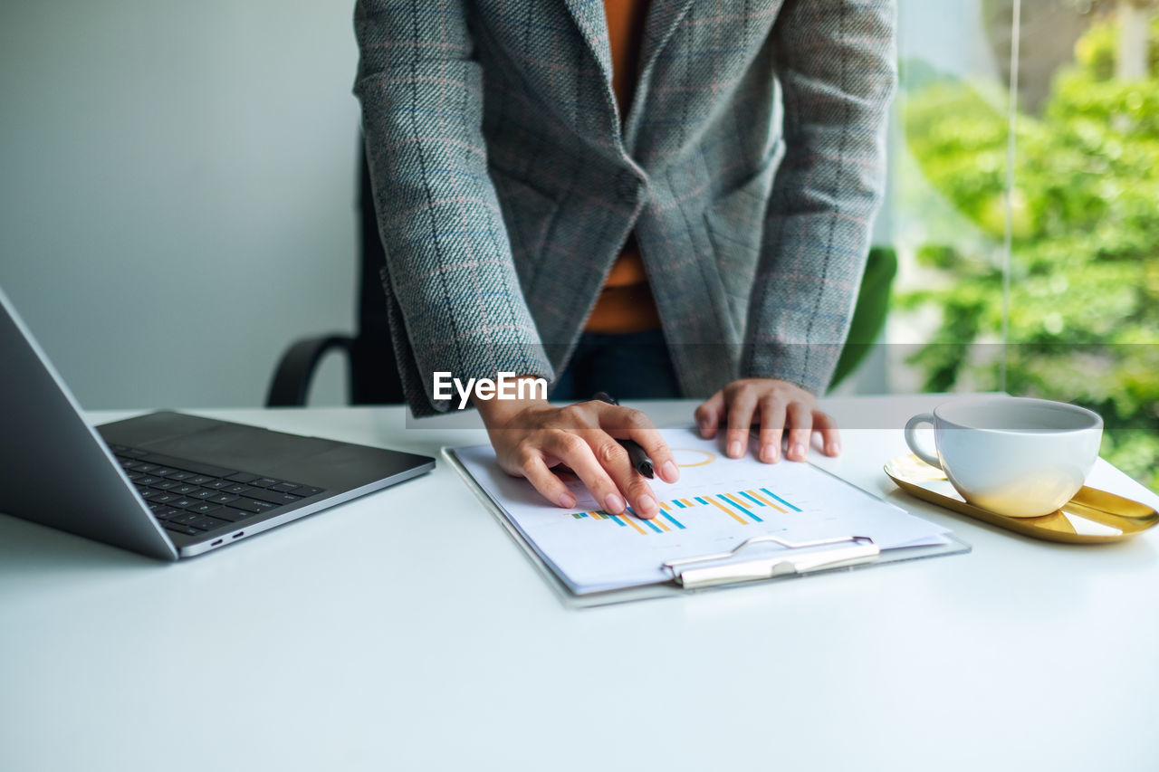 Midsection of businesswoman with laptop standing at desk