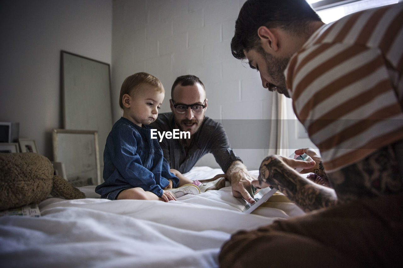 Fathers showing tablet computer to daughter while sitting on bed at home