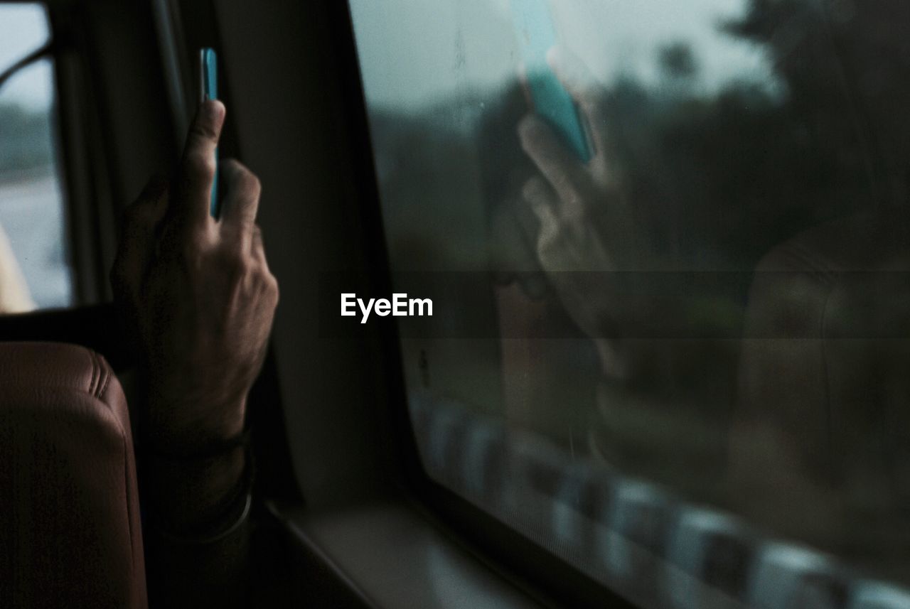 Cropped hand of man photographing by train window with mobile phone