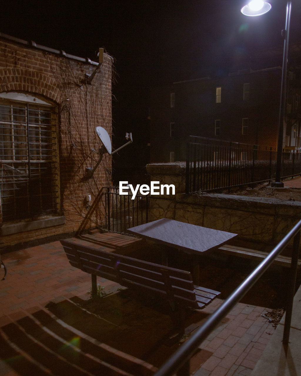 Empty bench by illuminated building at night