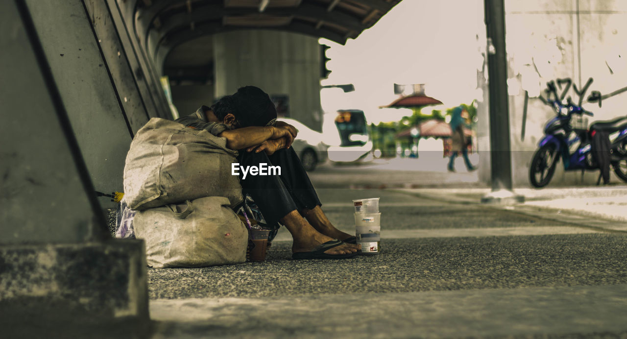 Beggar sitting under bridge