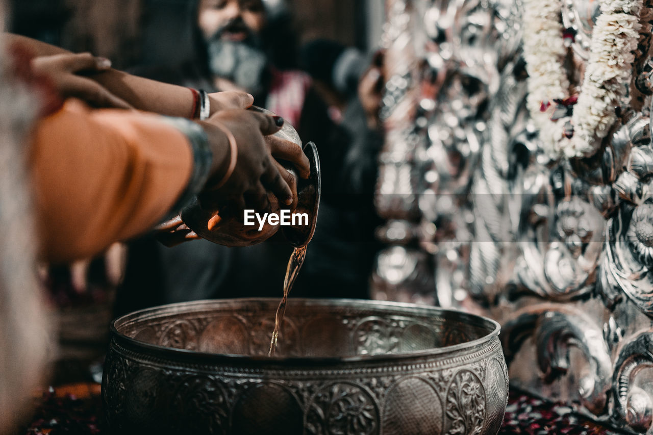 Close-up of people pouring water in utensil at temple