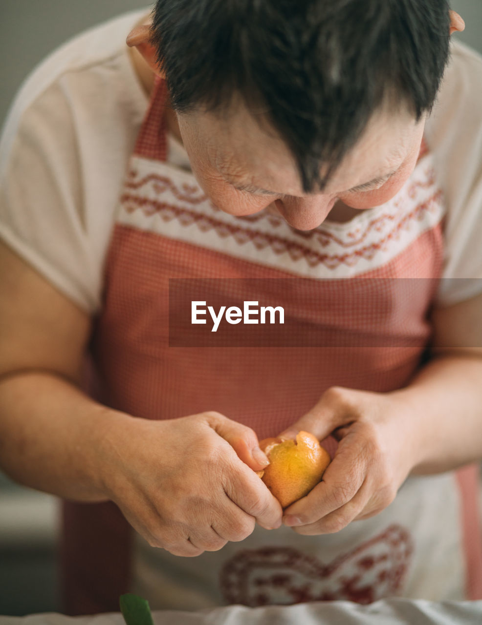 Lifestyle, education. elderly woman with down syndrome is studying in kitchen peel tangerine 