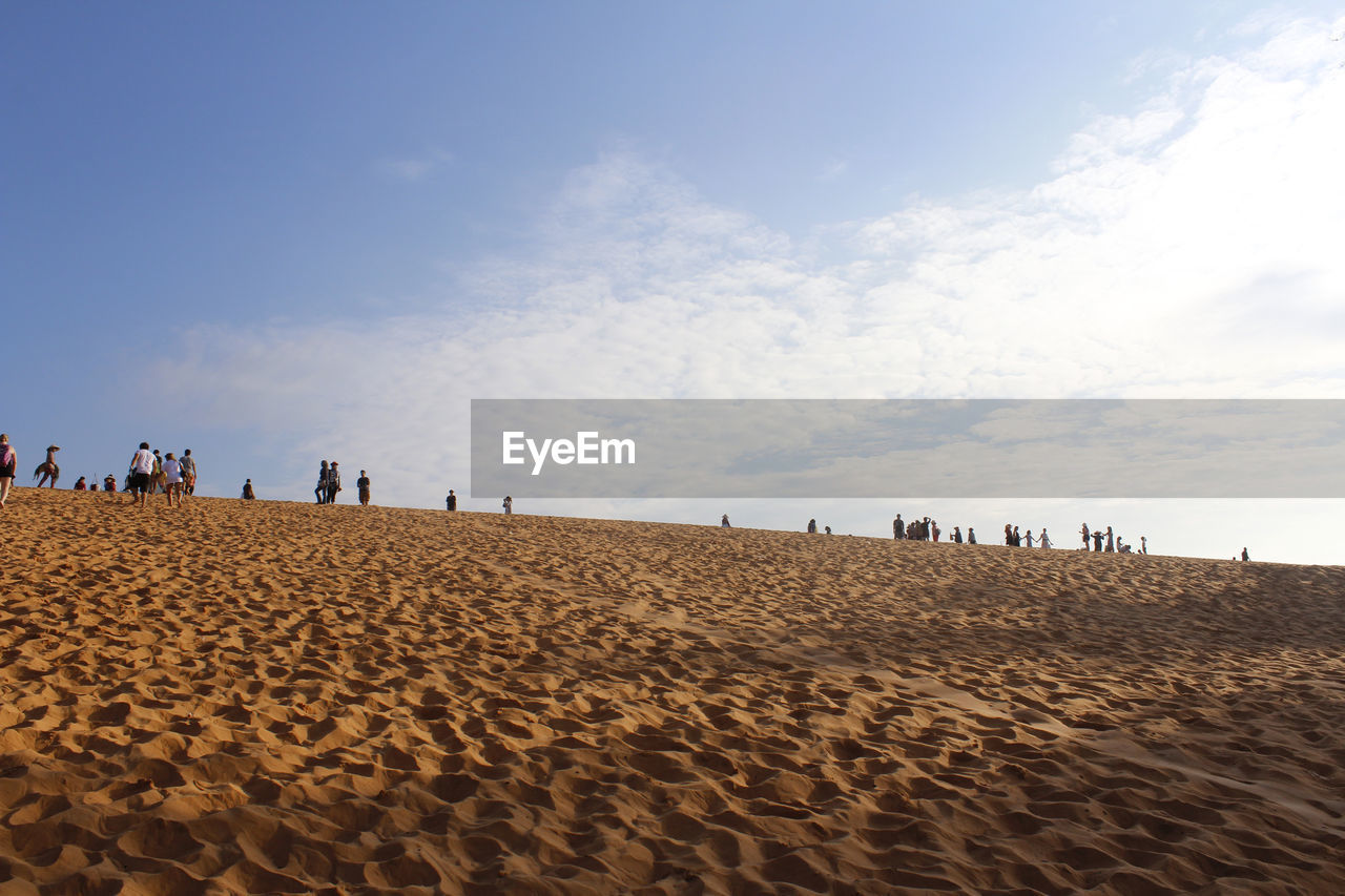 PEOPLE ON SAND AT BEACH AGAINST SKY