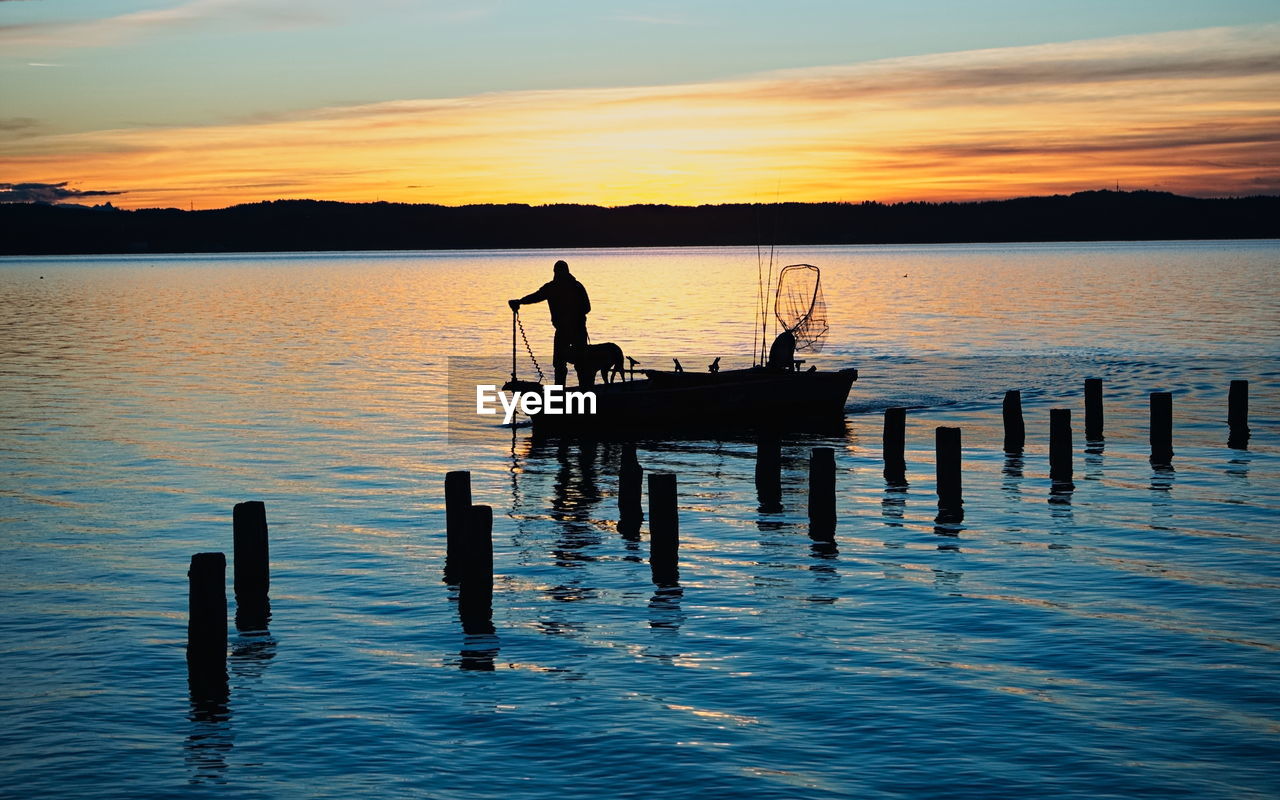 water, reflection, sunset, sea, sky, silhouette, horizon, ocean, dusk, evening, nature, shore, beauty in nature, transportation, men, tranquility, scenics - nature, cloud, bay, nautical vessel, tranquil scene, mode of transportation, wood, outdoors, post, two people, vehicle, wave, adult, pier, wooden post, fishing, orange color, lifestyles, idyllic, occupation, leisure activity, standing, coast, sunlight