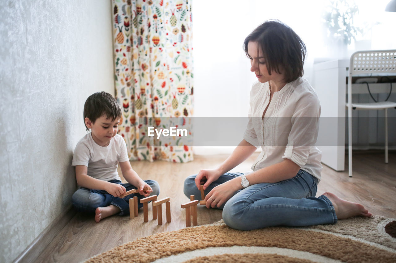 Joint game of mom and son at home, build houses from a wooden constructor. concept childhood 