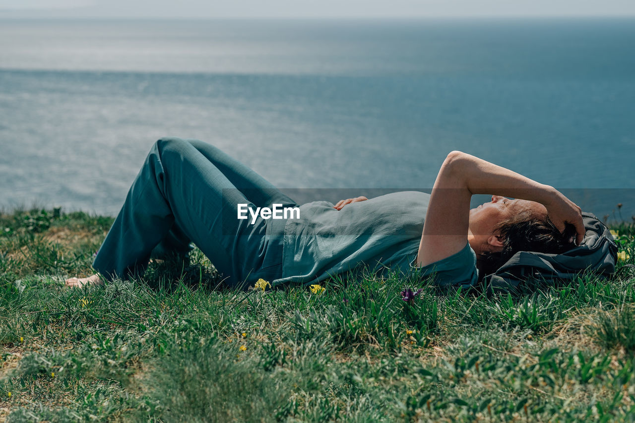 An adult woman, a pensioner, lies on the grass barefoot with a smile on her face on a sunny day