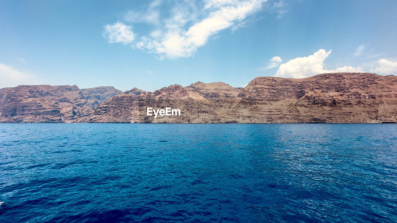 scenic view of sea by mountains against sky