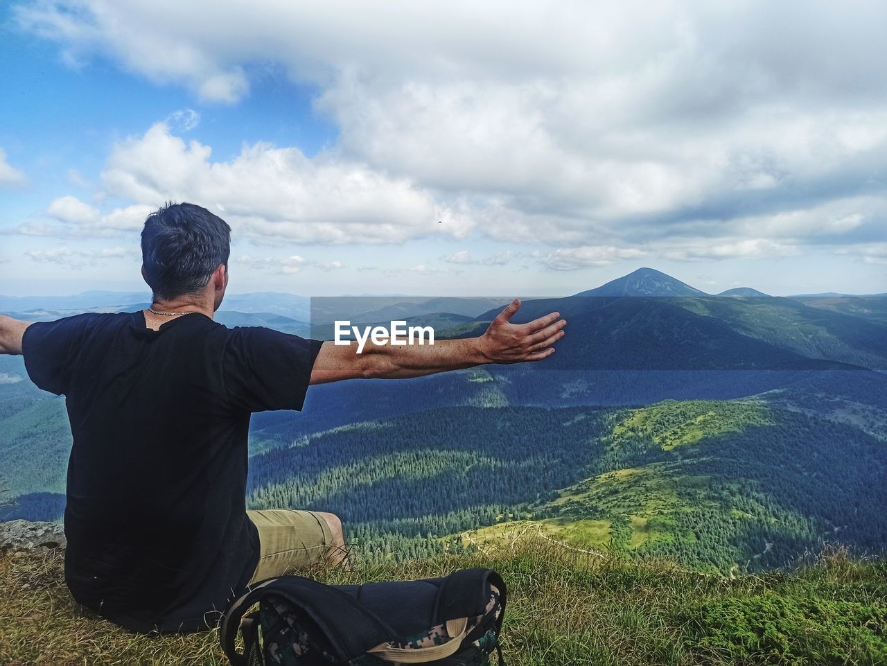 REAR VIEW OF MAN WITH ARMS RAISED AGAINST SKY