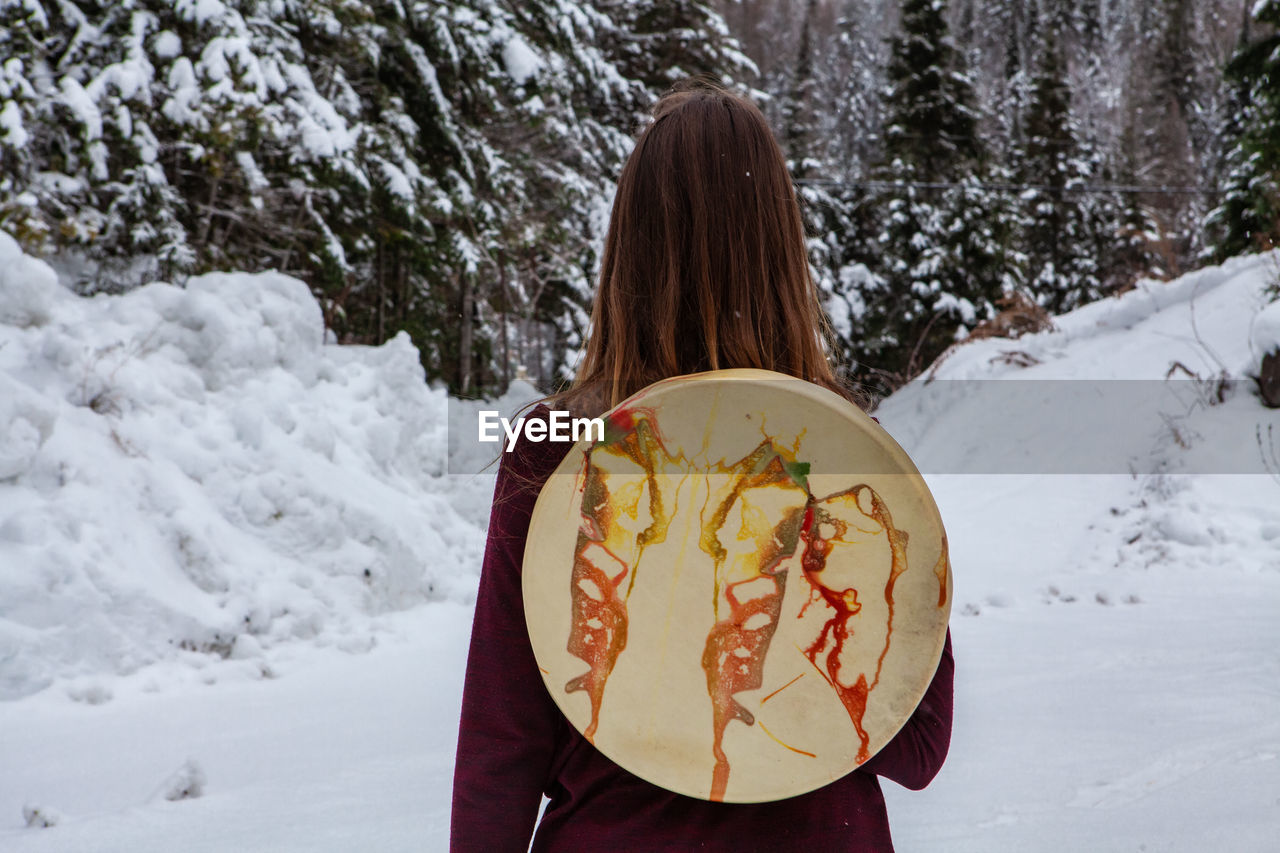 REAR VIEW OF WOMAN HOLDING ICE CREAM CONE AGAINST SNOW