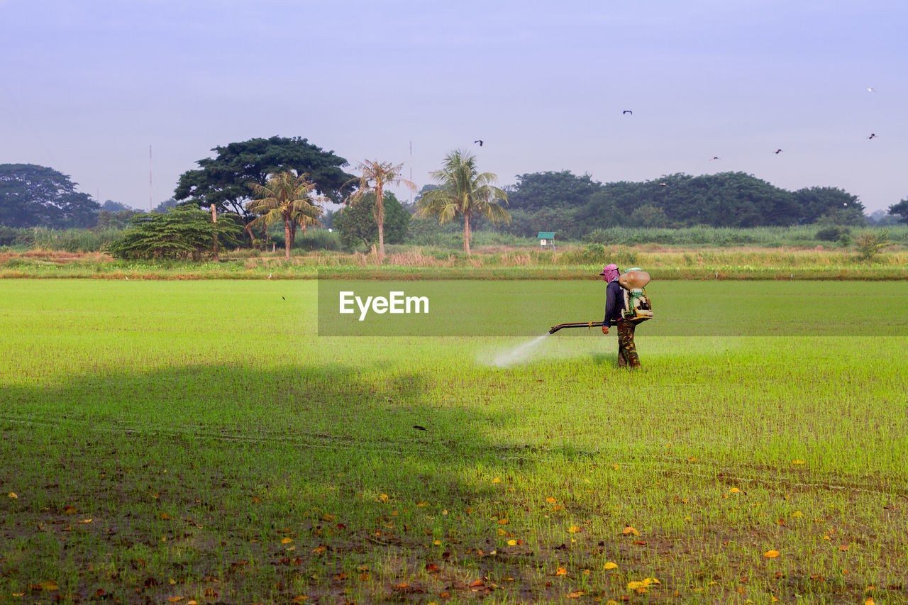 Farmer spraying fertilizer on field against sky