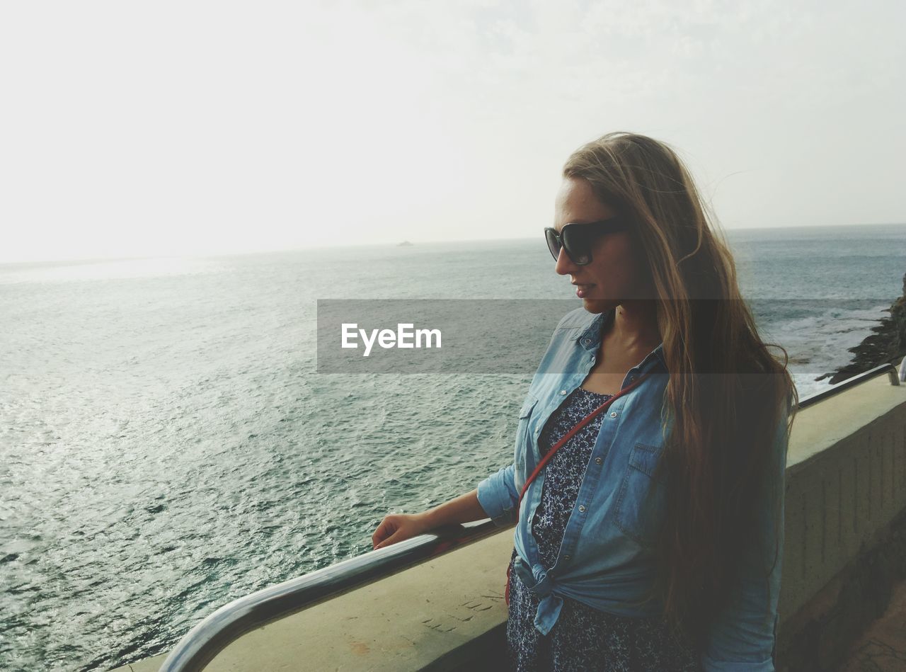 Woman standing by railing against clear sky