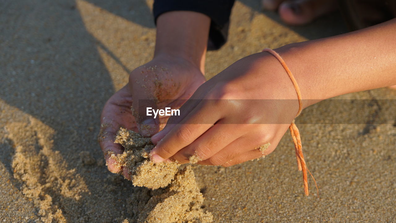 CLOSE-UP OF HANDS ON SAND AT BEACH