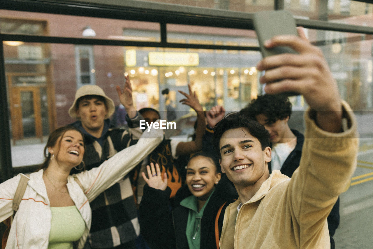 Happy man taking selfie with cheerful friends through smart phone at train station