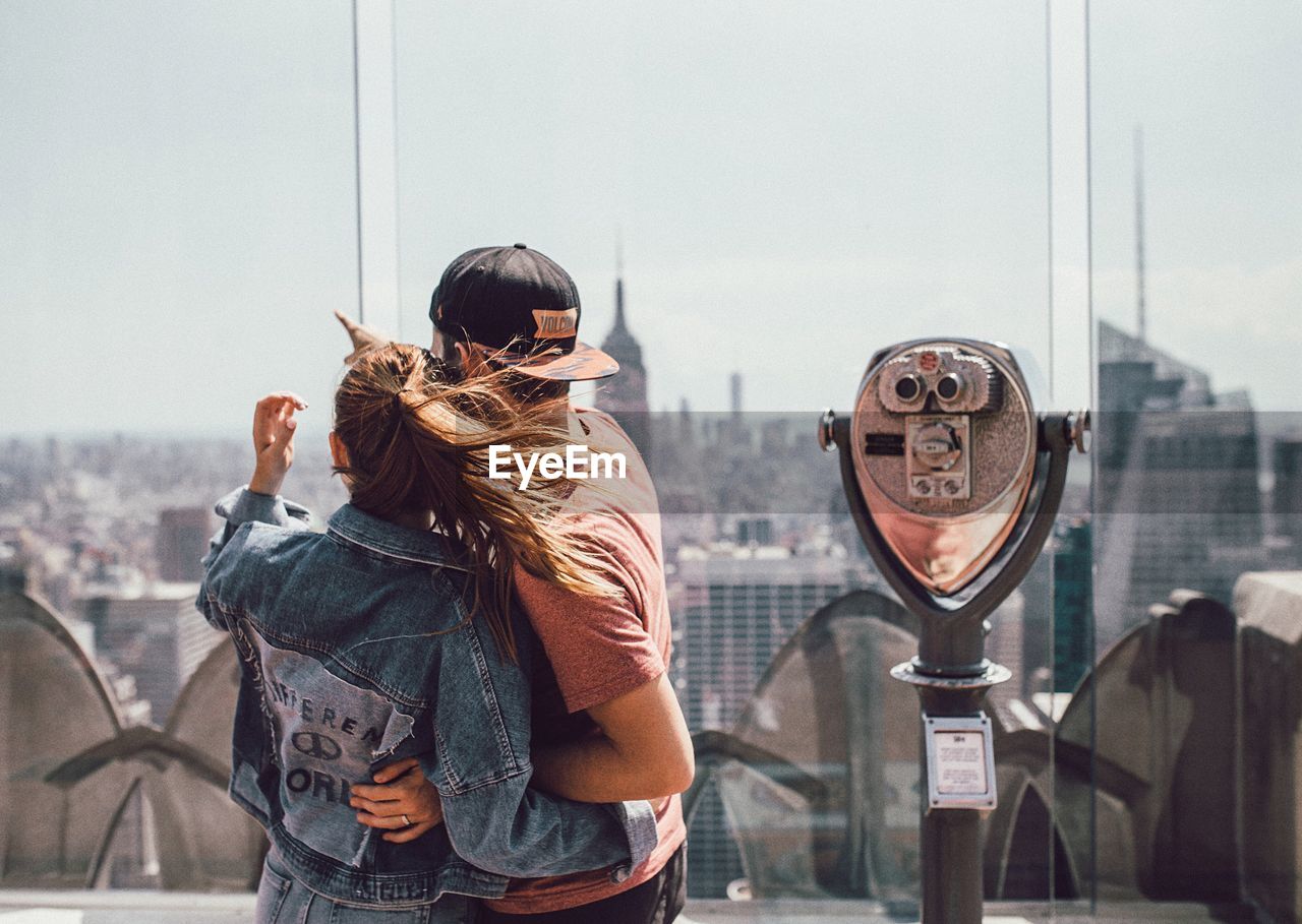 Rear view of couple looking at cityscape by coin-operated binoculars