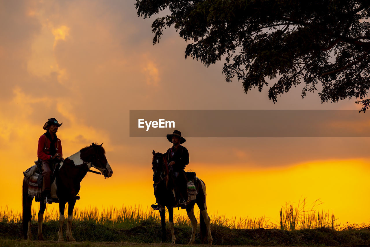 Three men dressed in cowboy garb, with horses and guns. a cowboy riding a horse in the sunset.