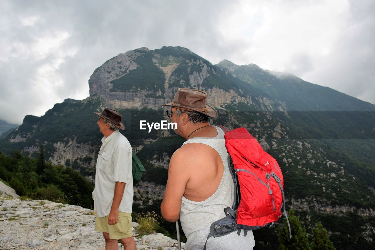 Male friends hiking on mountain against cloudy sky