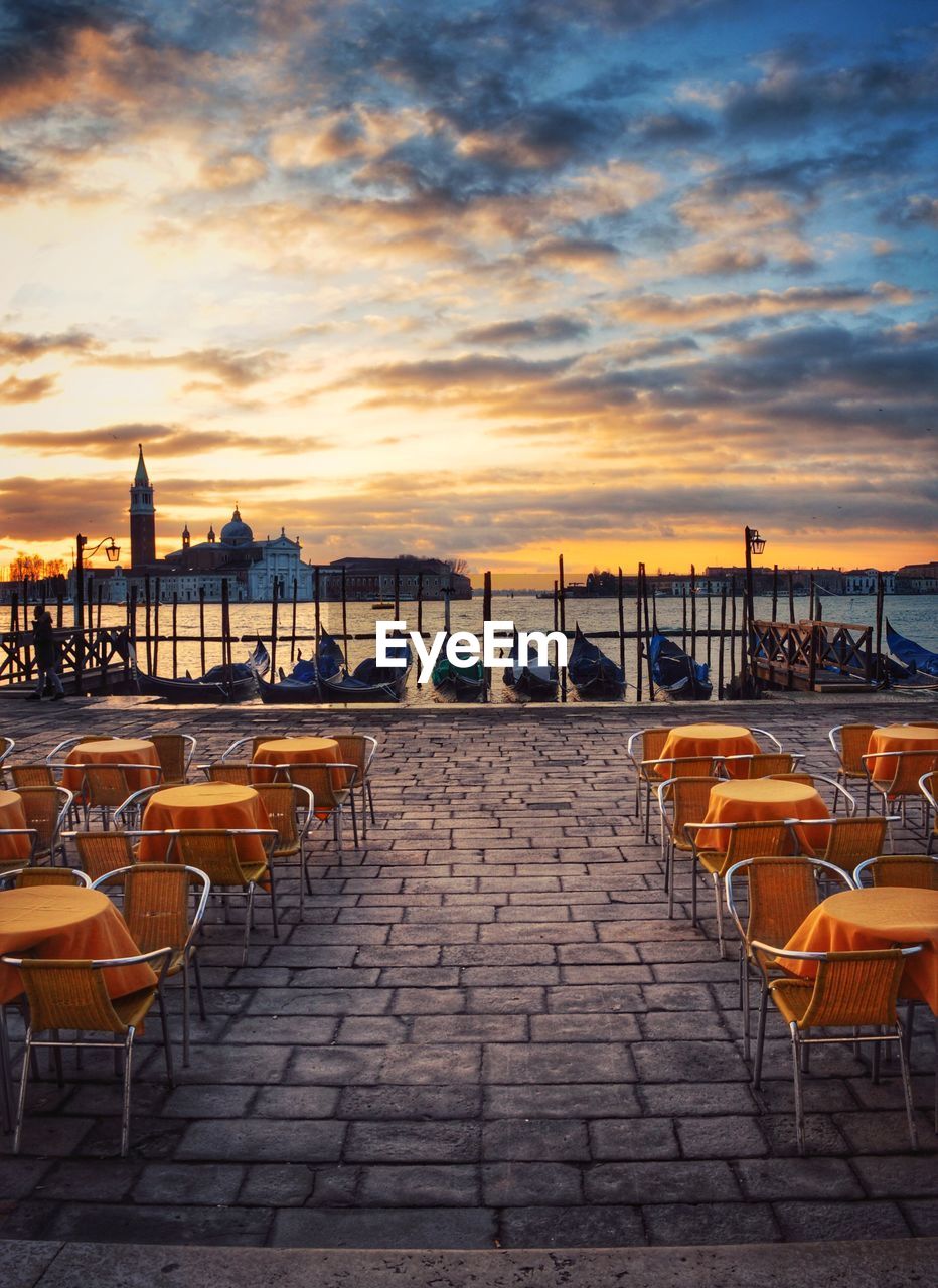 Empty chairs and tables against sky during sunset