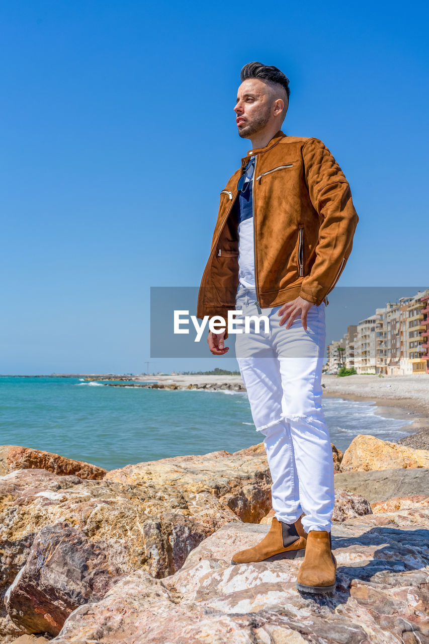 FULL LENGTH OF MAN STANDING ON SHORE AGAINST SEA