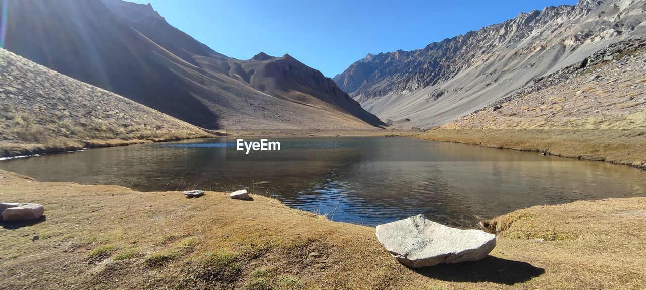 mountain, water, scenics - nature, landscape, environment, wilderness, beauty in nature, lake, nature, mountain range, sky, land, valley, reflection, travel destinations, travel, reservoir, tranquility, no people, sunlight, blue, rock, sunny, tranquil scene, mountain peak, clear sky, moraine, snow, outdoors, glacial lake, day, cold temperature, activity, non-urban scene, plant, glacial landform, tourism, geology, leisure activity, wadi, ice, plateau, snowcapped mountain, idyllic, winter, lakeshore