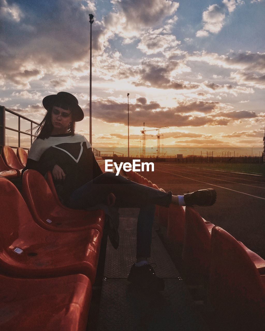 Woman sitting on chair in stadium against sky during sunset