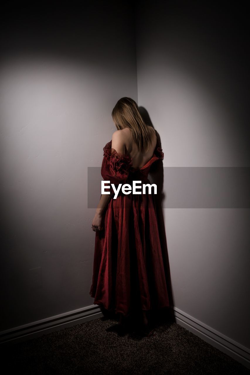 Rear view of woman standing by wall in darkroom