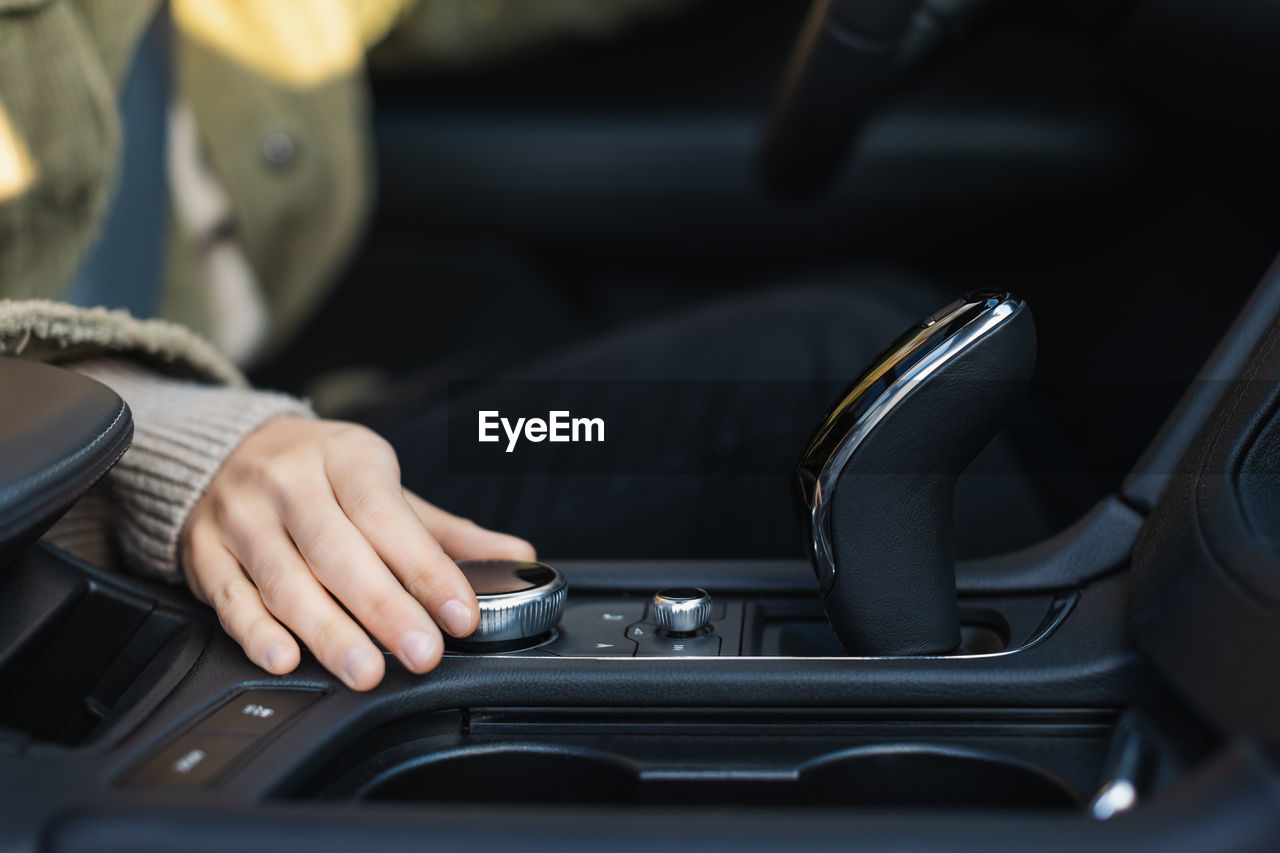 Young caucasian woman hand's turns the control wheel of a modern multimedia system in the car. 