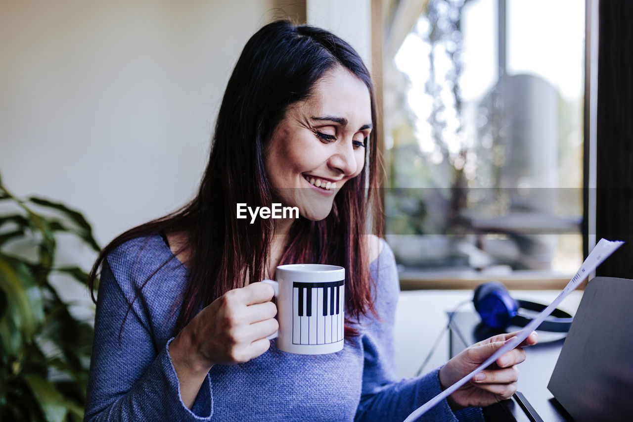 Happy woman with coffee cup holding sheet