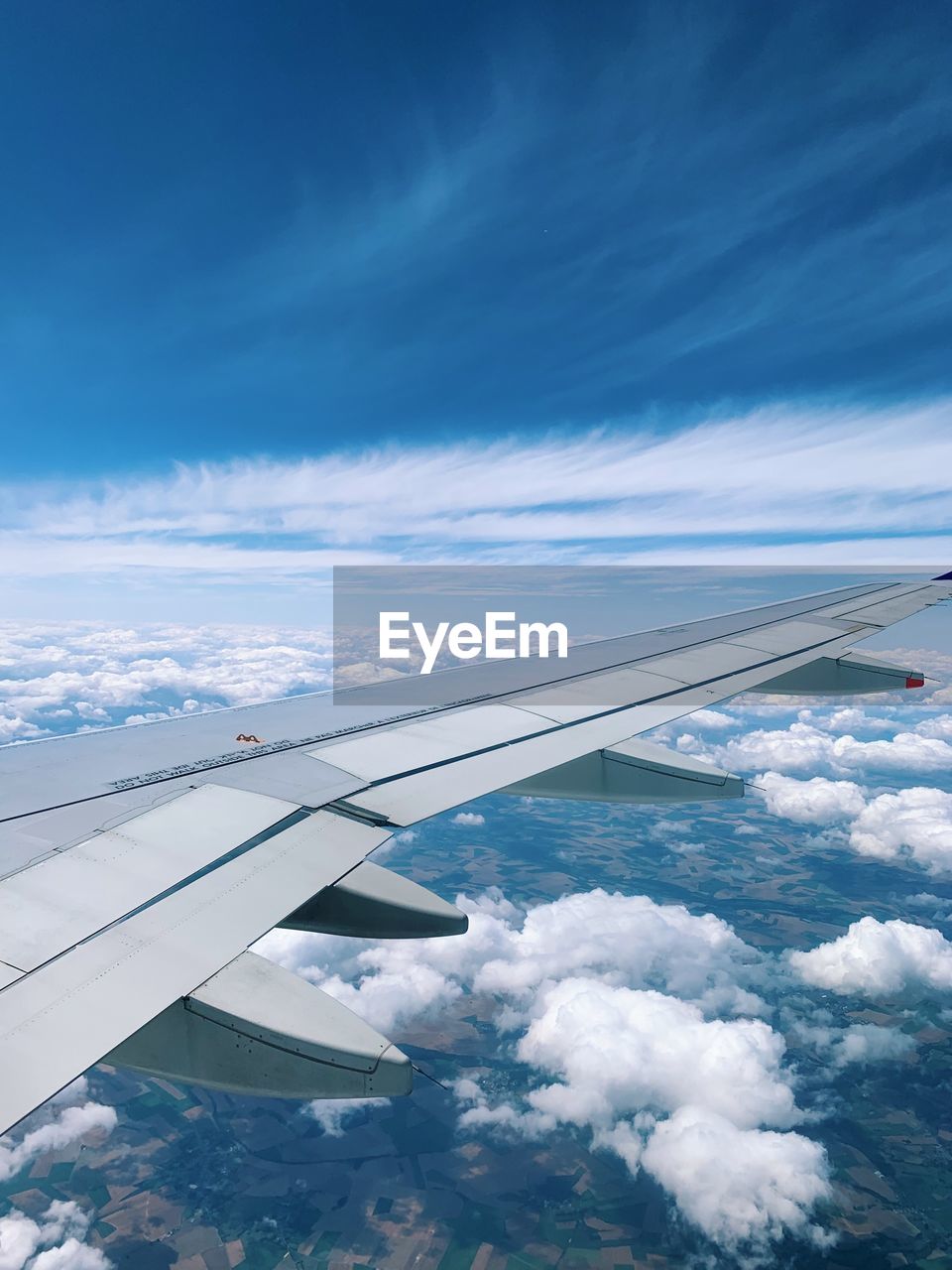 In the air, flying over the land and the clouds, traveling with a blue sky, airplane wing view 