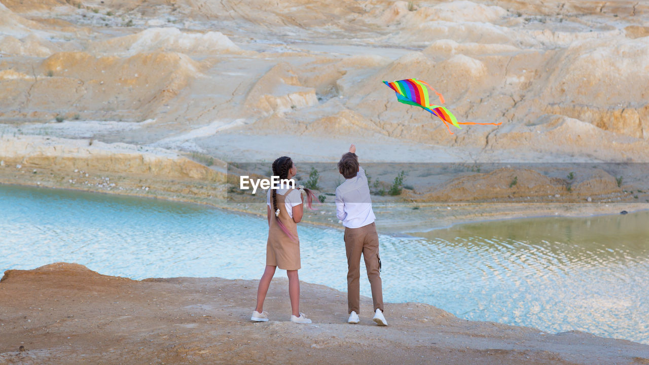 A boy and a girl launch a bright kite into the sky mountains near the river.