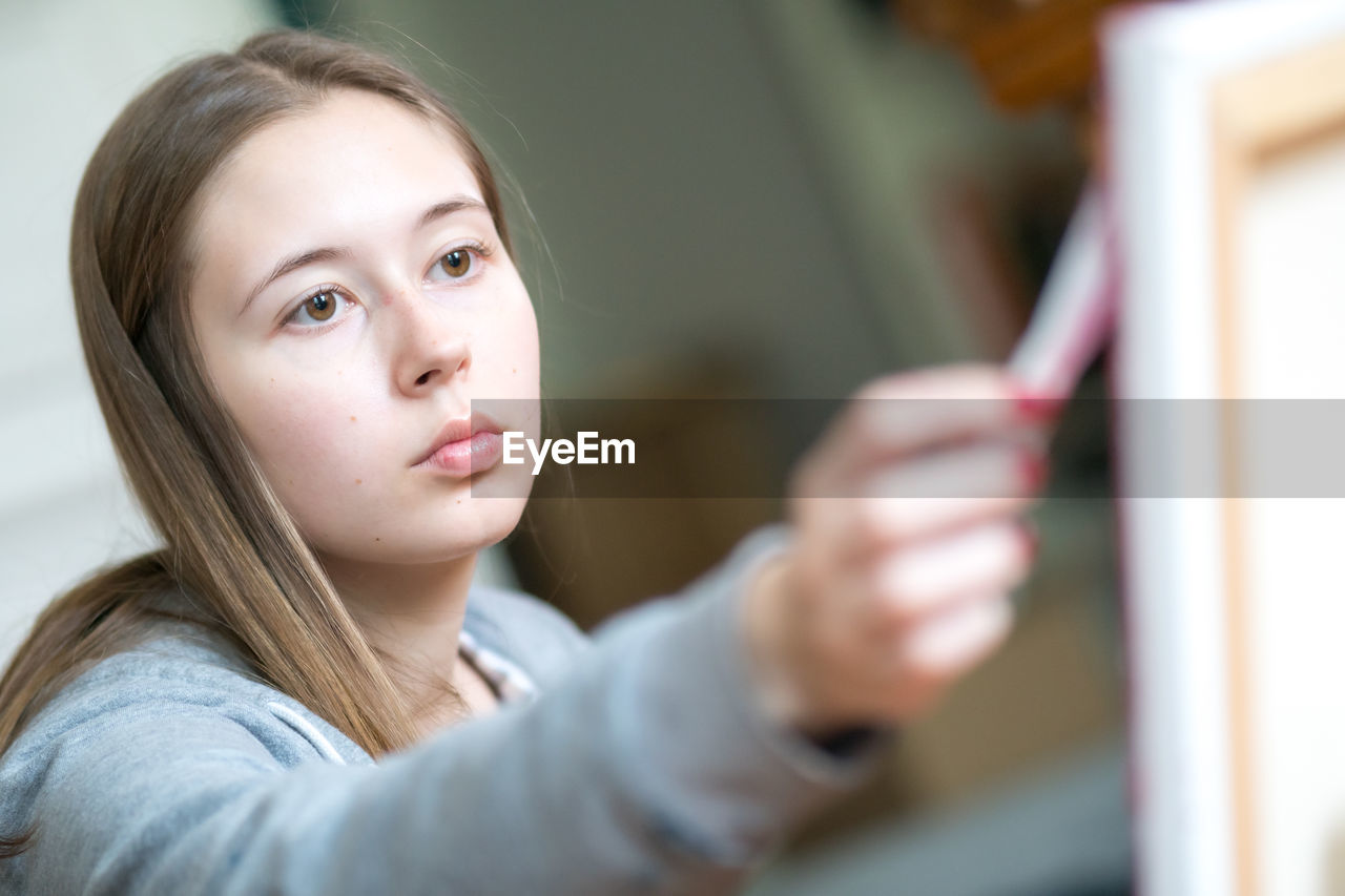 Concentrated young woman painting on canvas