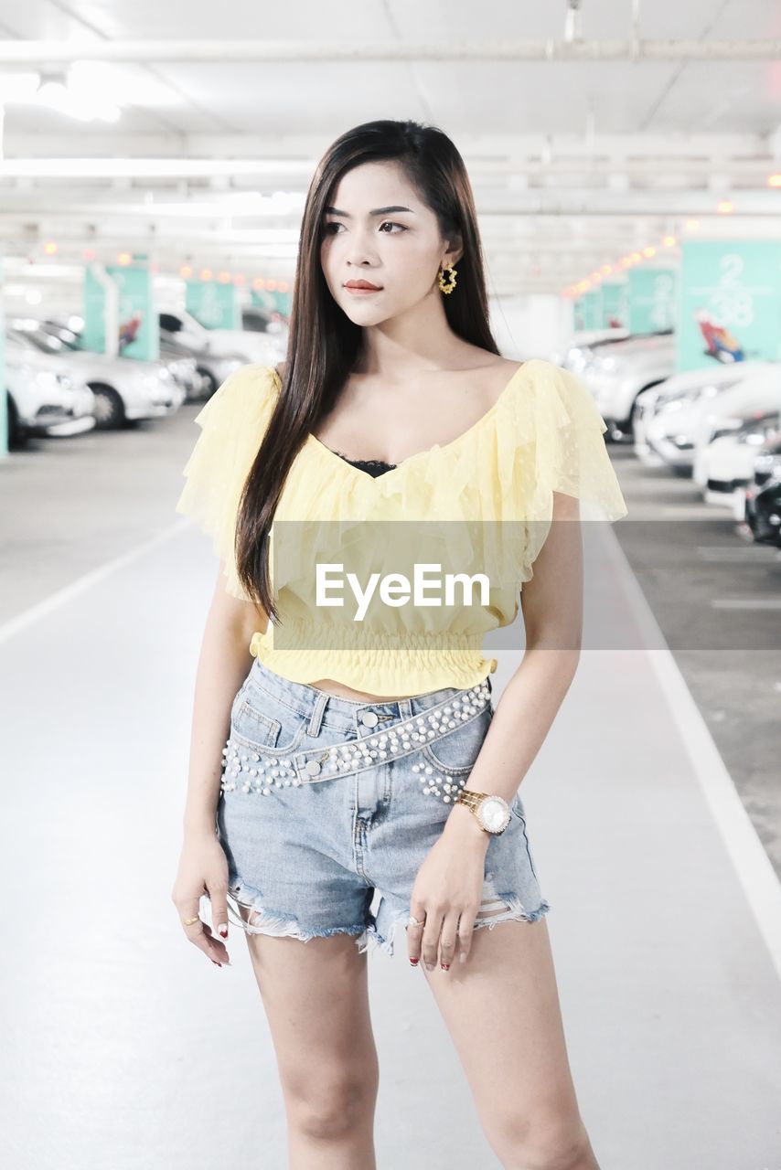 Beautiful young woman looking away while standing in parking lot