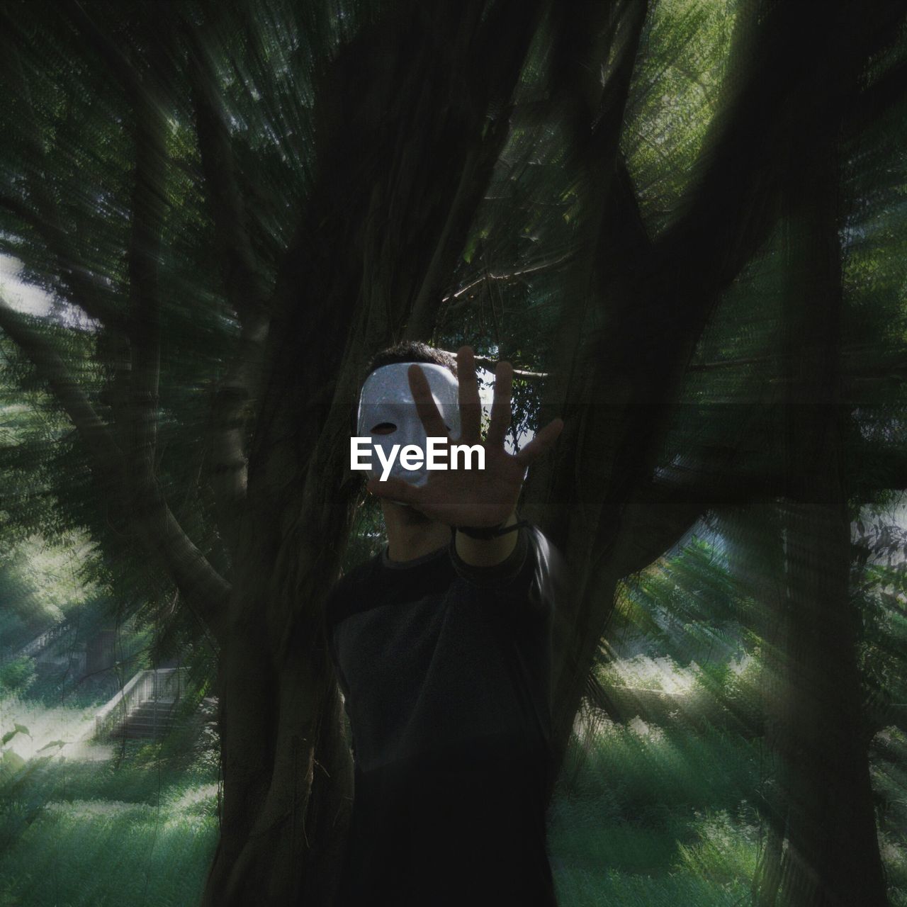 Man wearing mask while standing against tree