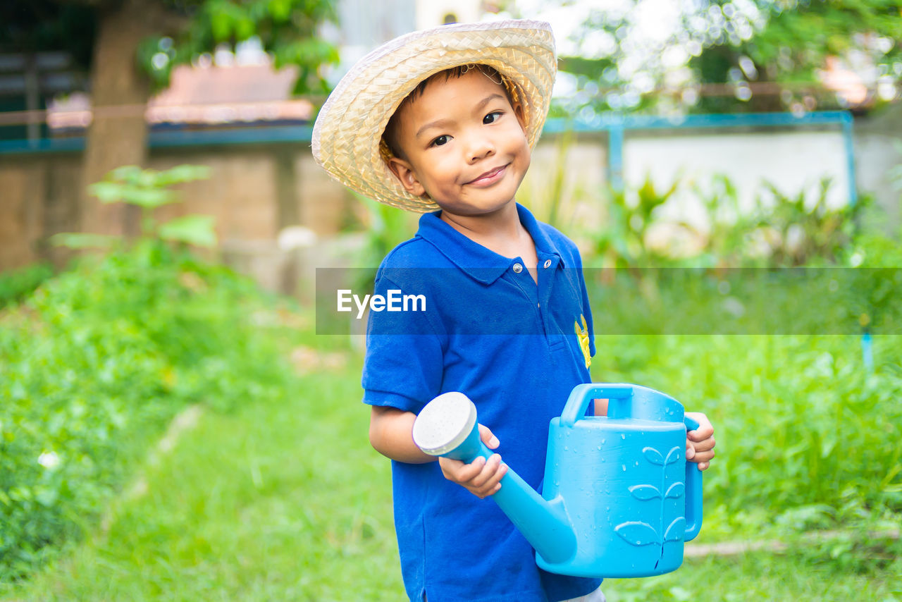 Portrait of smiling boy holding watering can while standing on land