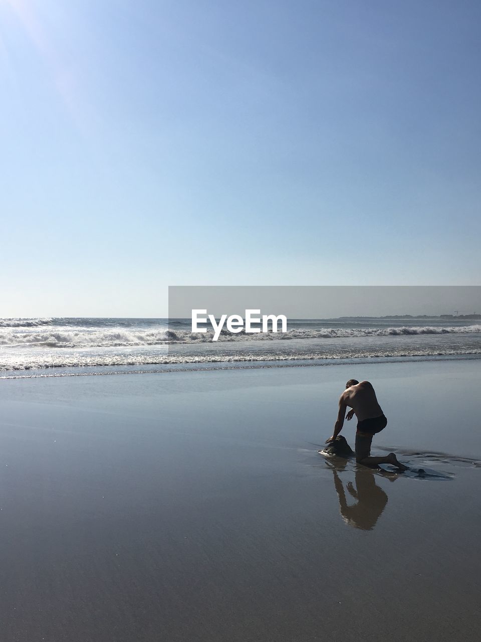Rear view of woman kneeling on beach against clear sky