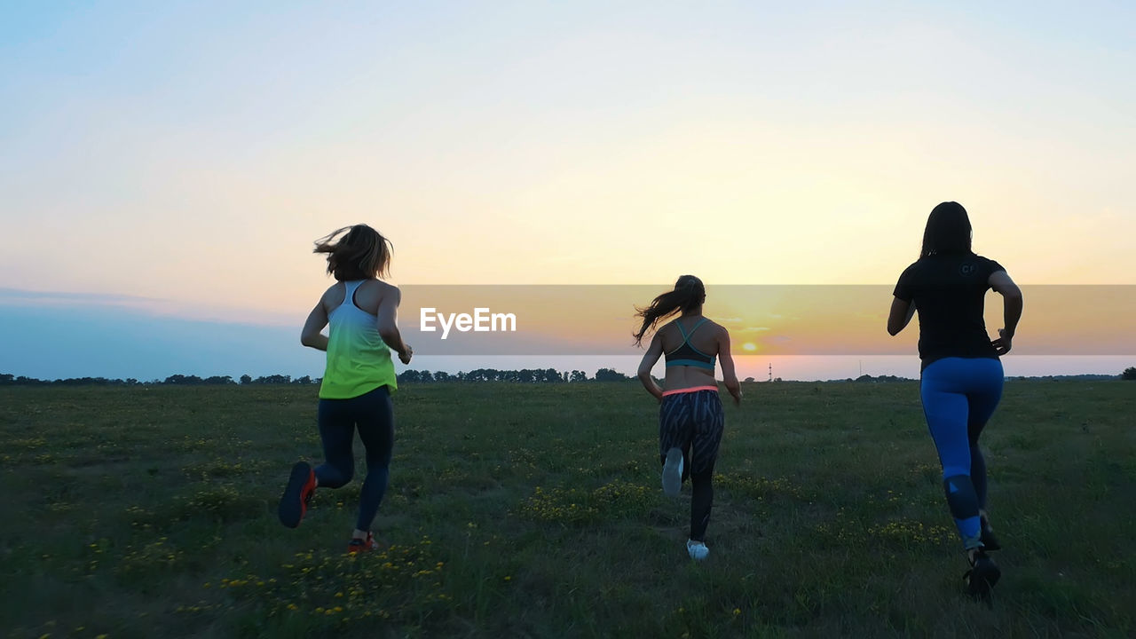 Young women in sunglasses, in tights, run synchronously along the green meadow, field. in summer